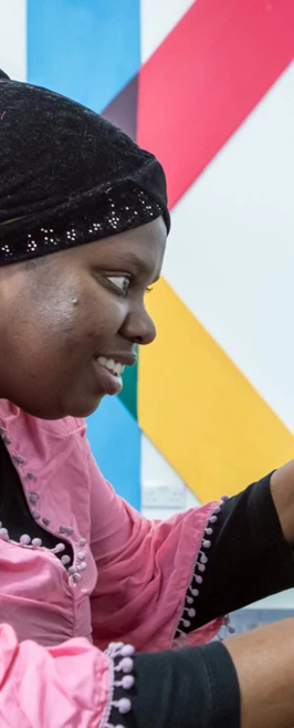 Student in a pink top working on assembling a small blue robotic vehicle, adjusting its wheels on a table. Student in a pink top working on assembling a small blue robotic vehicle, adjusting its wheels on a table.